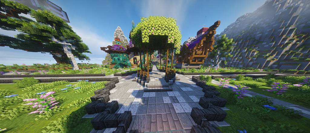 Il viale dello spawn: un gazebo coperto di foglie tra case fantasy, prati fioriti e montagne.